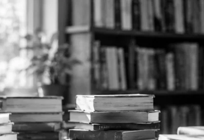 Stacks of books on a table in front of a wall of library shelves